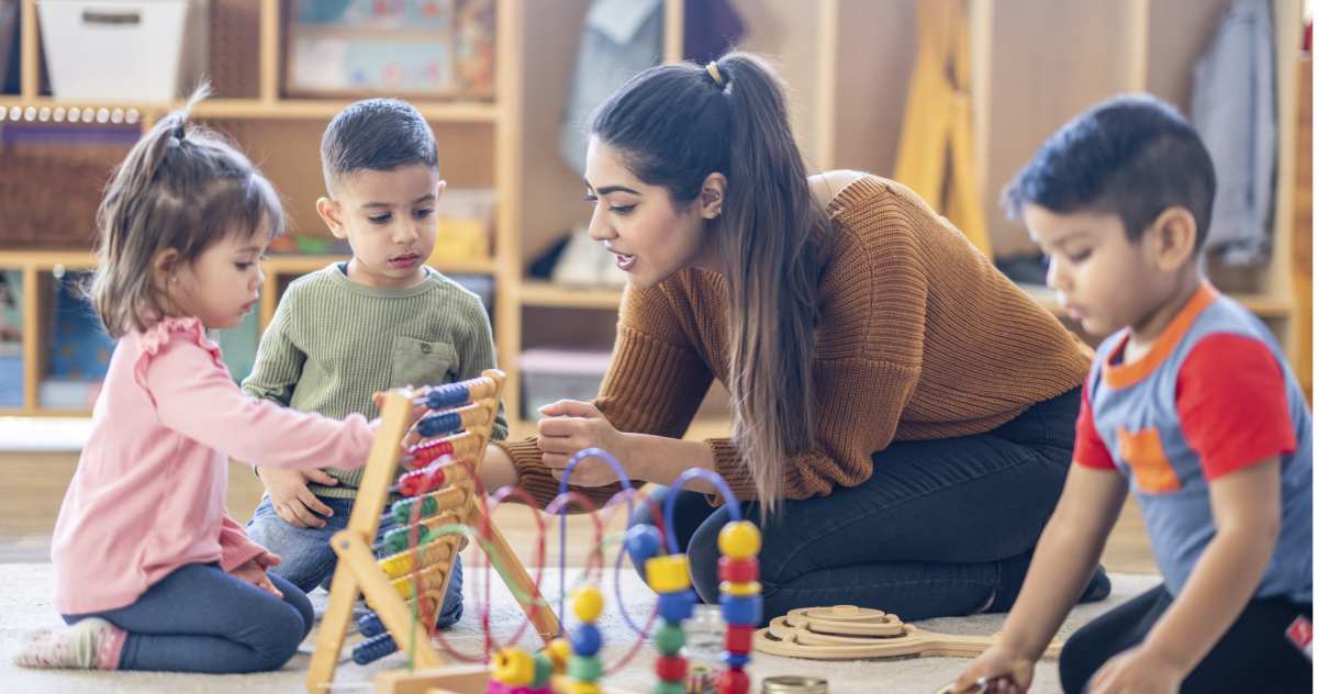 Adult playing with 3 young children on the floor with toys