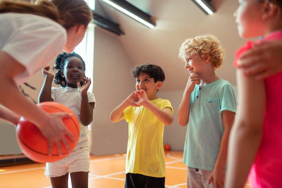 4 children about 7 years old in a circle playing basketball. One of the children is holding the ball about to bounce it.