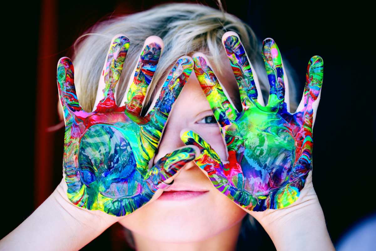 child holding their hands up which has colour swirls on them