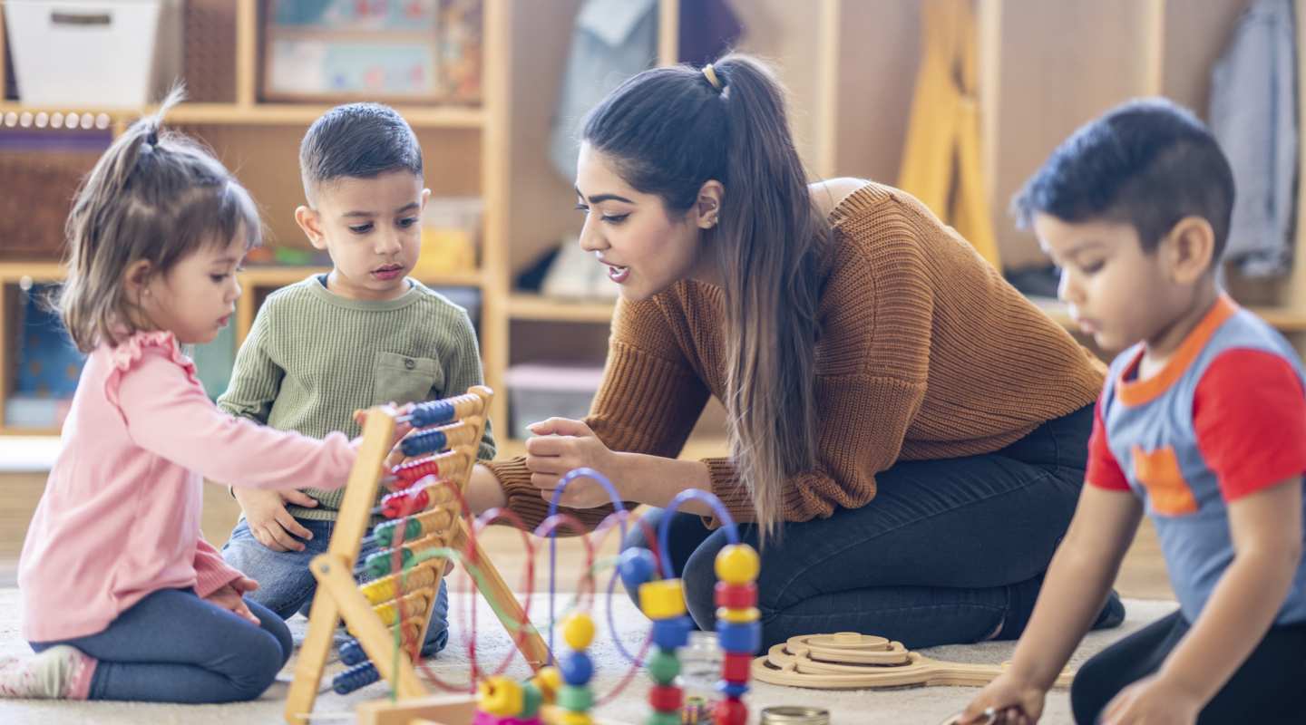 Adult playing with 3 young children on the floor with toys