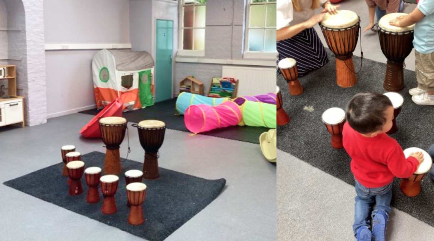 A room with drums toys, with a child in red sweater and jeans playing with drums in a playroom