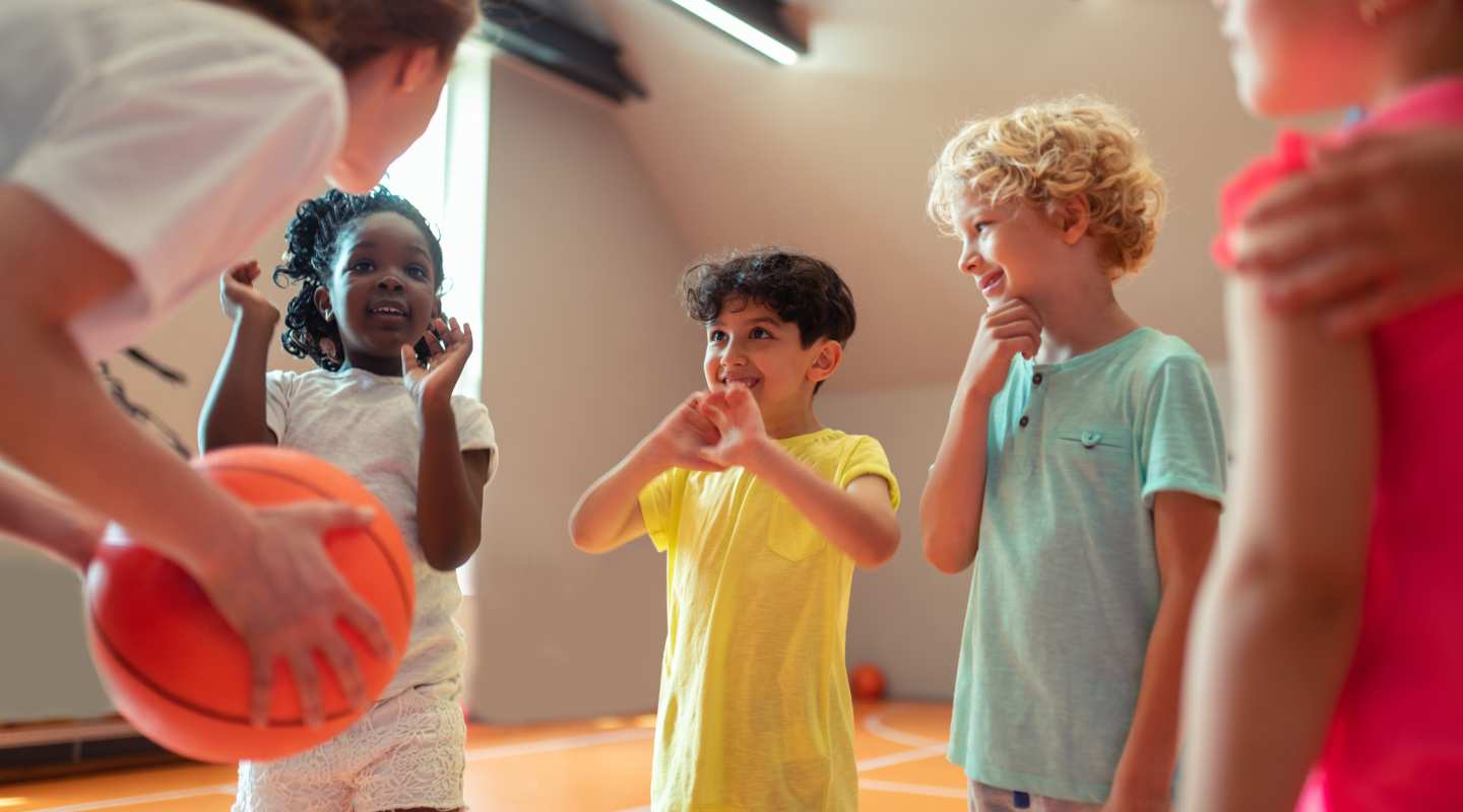 4 children about 7 years old in a circle playing basketball. One of the children is holding the ball about to bounce it.