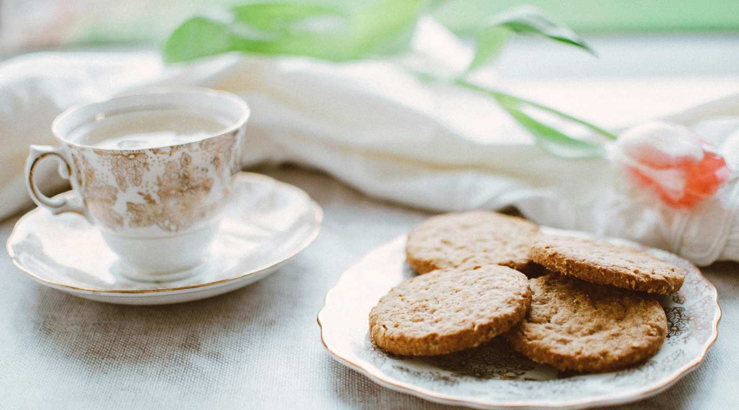 tea cup full of tea with a saucer on a table with a small plate of biscuits