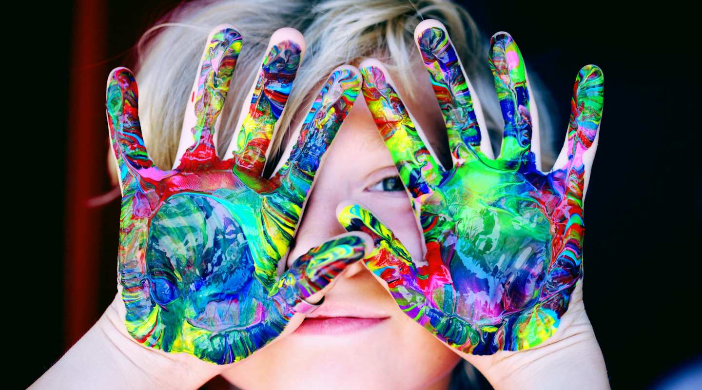 child holding their hands up which has colour swirls on them